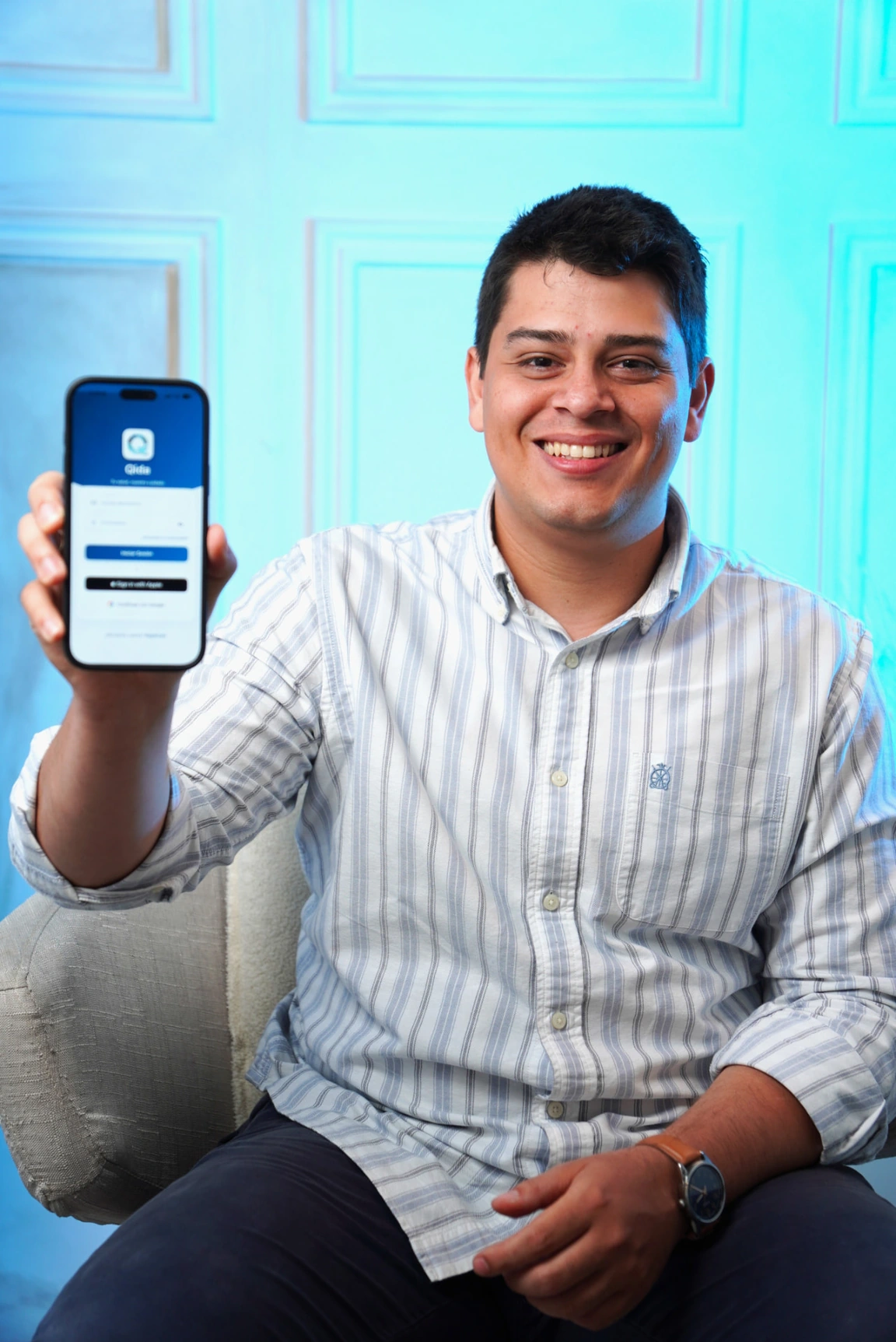 Joseph Corona smiles while holding up a phone displaying Qida.